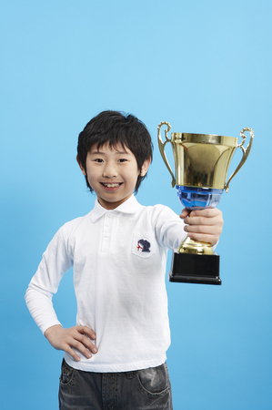 Young Asian boy posing in a studio with a trophyの写真素材