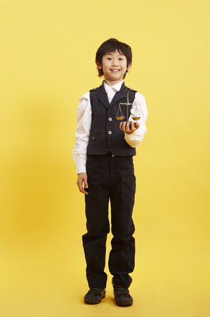 Young Asian boy in school uniform posing in a studio with justice scaleの写真素材