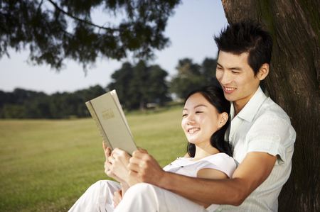 Asian couple posing together in a green field with a bookの写真素材