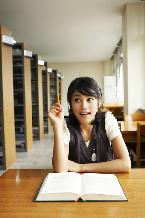 Female Asian college student posing in a library as sitting at deskの写真素材