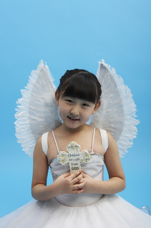 Young Asian girl wearing angel costume posing in a studio with crossの写真素材