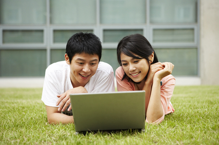 Asian college couple posing in the lawn field with laptopの写真素材