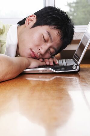 Male Asian college student posing in a library taking a nap with laptopの写真素材