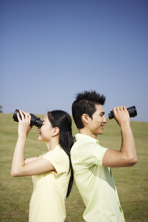 Asian couple posing together in a green field with binocularsの写真素材