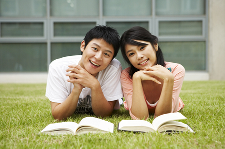 Asian college couple posing in the lawn field with booksの写真素材