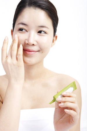 Cloes up shot of female Asian applying skincare products on face isolated in white backgroundの写真素材