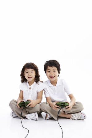 Young Asian boy and girl posing together in a studio with game joysticksの写真素材