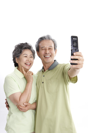 Asian elderly couple posing in a studio with cell phoneの写真素材