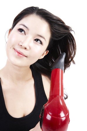 Female Asian doing her hair isolated in white background studio with hair dryerの写真素材