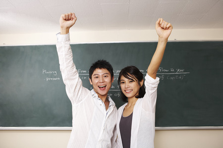 Asian college couple posing in a classroom with hand gestureの写真素材