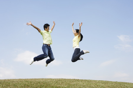 Asian couple posing together in a green field as jumpingの写真素材