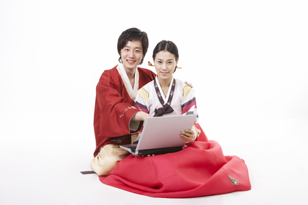 Asian couple wearing traditional korean costume posing in a studio with laptopの写真素材