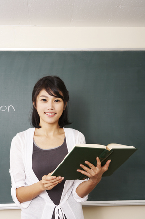 Female Asian college student posing in a classroom as standing in front of black boardの写真素材
