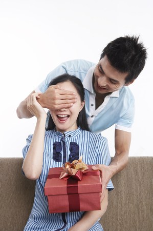 Asian couple sitting on a couch isolated in white background with giftboxの写真素材