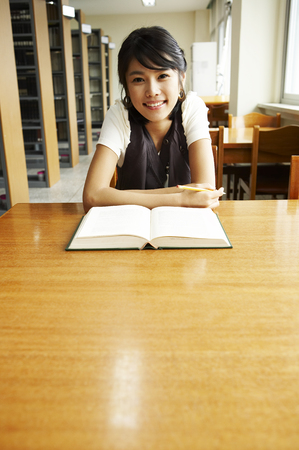 Female Asian college student posing in a library as sitting at deskの写真素材