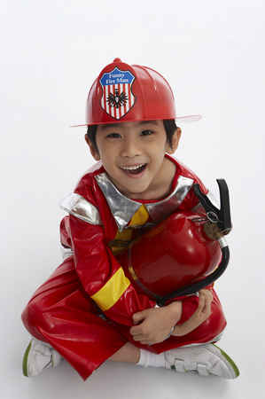 Young Asian boy wearing firefighter uniform posing in a studio with fire extinguisherの写真素材