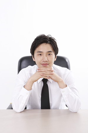 Asian business man in suit posing in a studio as sitting at deskの写真素材