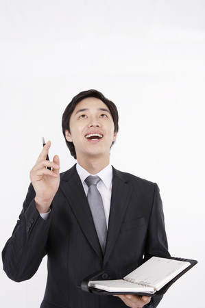 Asian business man in suit posing in a studio with pen and notebookの写真素材