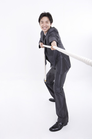 Asian business man in suit posing in a studio as playing a tug of warの写真素材