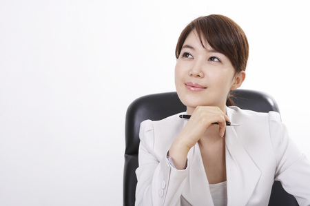 Asian business woman in suit posing in a studio as sitting at deskの写真素材