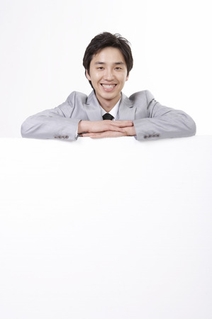 Asian business man in suit posing in a studio peeking from behind the wallの写真素材