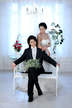 Asian bride and groom in wedding dresses posing in a studio as sitting down with a bouquet of flowersの写真素材