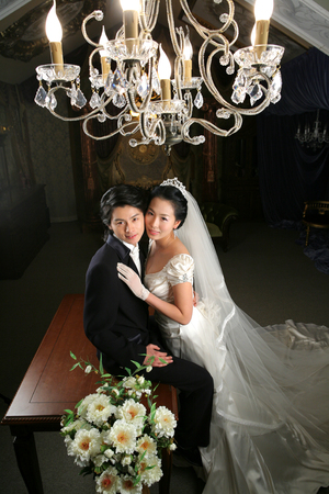 Asian bride and groom in wedding dresses posing in a studio under chandeliersの写真素材