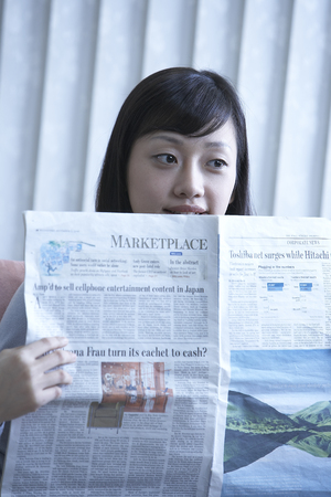 Asian woman sitting on a chair by the window with newspapersの写真素材