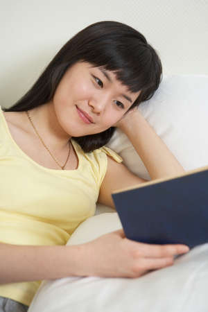 Asian woman resting on bed as reading a book