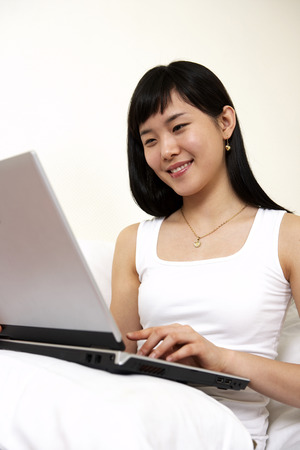 Asian woman resting on bed as using laptopの写真素材