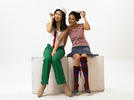 Two Asian women fashion models posing in a studio as sitting on a cube boxの写真素材