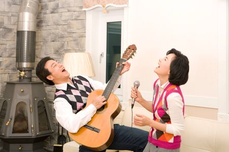 Mid-aged married Asian couple spending time together with guitar in the living roomの写真素材