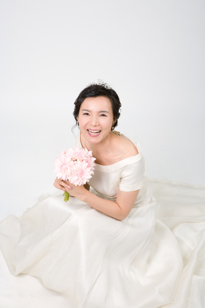 Mid-aged Asian woman posing in a studio as wearing wedding dressesの写真素材