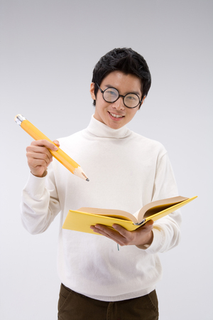 Young Asian man wearing glasses posing with a yellow book and pencil - isolated on whiteの写真素材