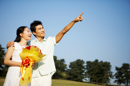 Young Asian couple posing with a bunch of flowers in the parkの写真素材
