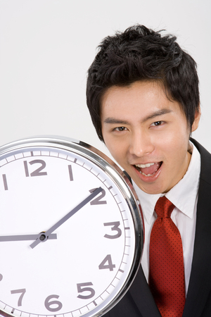 Young Asian businessman posing with a clock - isolated on whiteの写真素材