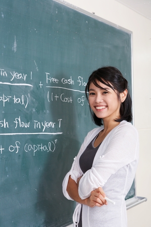 Asian female English teacher standing in front of black boardの写真素材