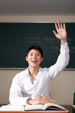 Asian male student holding up his hand in the air in the classroomの写真素材