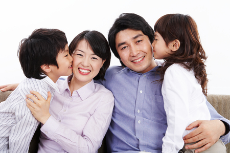 Young Asian son and daughter kissing on the parents' cheeks - isolated on whiteの写真素材