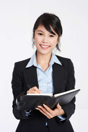 Young enthusiastic Asian business woman writing on her scheduler and smiling - isolated on whiteの写真素材