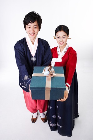 Young Asian couple in Hanbok, Korean traditional attire posing with a gift box - isolated on whiteの写真素材
