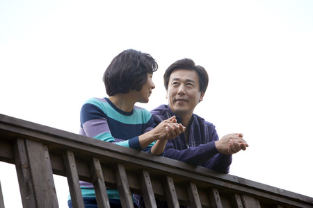 Asian middle aged couple leaning on the wooden bridge and happily talking to each otherの写真素材