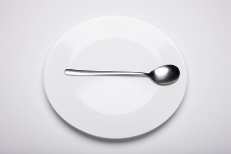 Spoon on an empty plate - isolated on whiteの写真素材