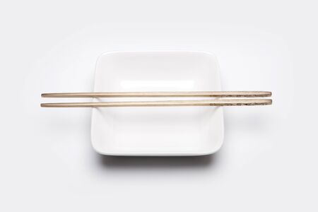 Metal chopsticks on small white plate - isolated on whiteの写真素材