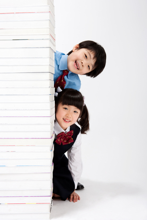 Asian boy and girl with smile behind the pile of books isolated on whiteの写真素材