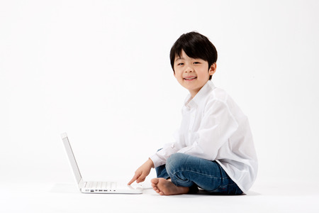 Asian boy using laptop sitting on floor isolated on whiteの写真素材