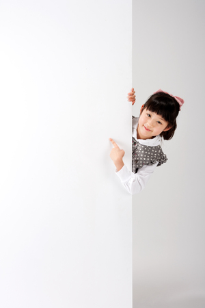 Asian girl pointing something behind the wall isolated on whiteの写真素材