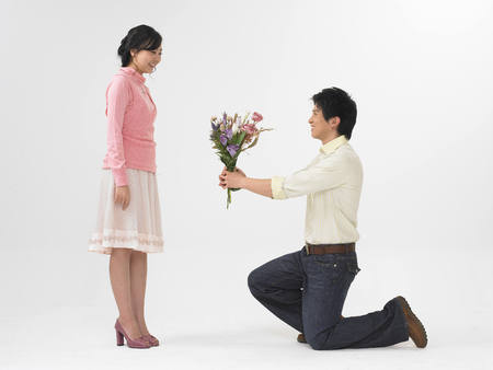 Asian young man proposes to girlfriend giving flower isolated on whiteの写真素材