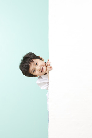 Asian cute boy hiding behind white board on mint backgroundの写真素材