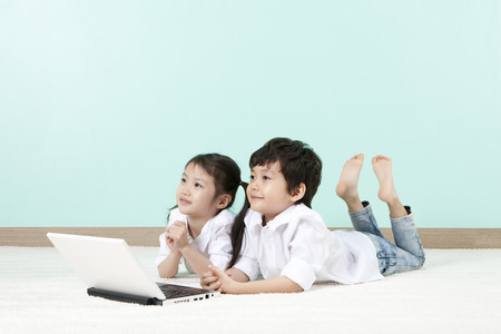 Asian cute boy and girl using laptop lying on the floorの写真素材